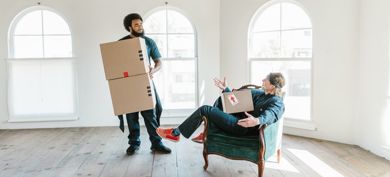 Two movers Sherman Oaks talking in a room while holding carton boxes.